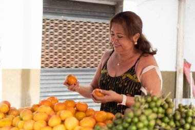 Gülümseyen kadın açık hava meyve tezgahında olgun mandalinaları seçiyor.