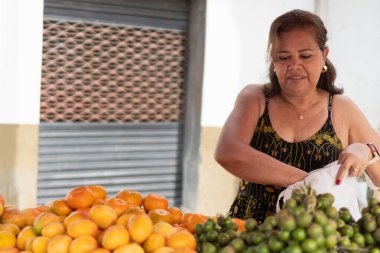 Açık pazarda taze meyve satan bir kadın, ürünleri torbaya koyuyor.