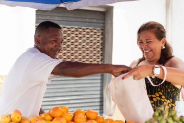 Pazarcı ve müşteri, sokak tezgahından taze meyve alırken mutlu bir şekilde etkileşime giriyorlar.