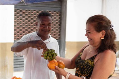 Sokak satıcısı gülen bir müşteriyle etkileşime geçip taze tropikal meyve alıyor.