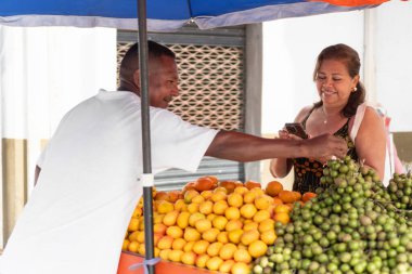 Bir kadın açık hava pazarında tropik meyveler için dijital ödeme yapıyor.