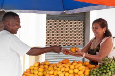 Gülümseyen satıcı açık hava meyve standında müşteriye portakal satıyor.