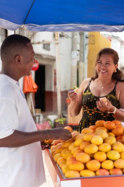 İnsanlar açık hava pazarında taze meyvenin tadını çıkarıyorlar, gülüyorlar ve etkileşime geçiyorlar.