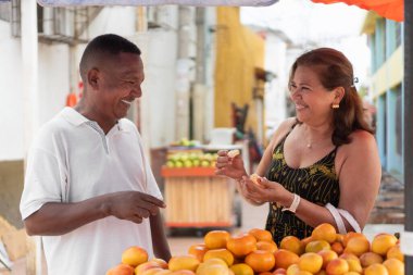 Bir kadın ve erkek, sokak satıcılarından taze portakal alırken gülümsüyor.