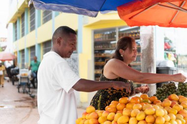Müşteriler yerel bir marketteki tezgahtan taze tropikal meyve seçiyorlar.