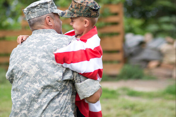Happy family reunited father soldier and his son holding american flag outdoors tender scene