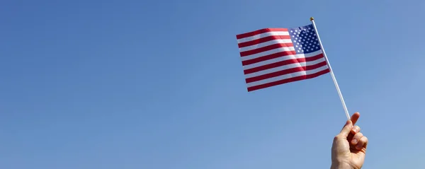 Boy hand holding American flag against  blue sky