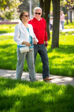 Neşeli son sınıf çifti şehir parkında eğleniyor, yürüyor, gülüyor ve güneşli günün tadını çıkarıyor. Yaşlı insanlar renkli kıyafetler giyiyorlar güneş gözlüğü takıyorlar.