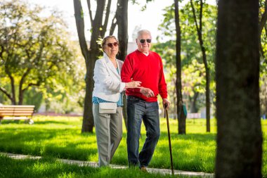Neşeli son sınıf çifti şehir parkında eğleniyor, yürüyor, gülüyor ve güneşli günün tadını çıkarıyor. Yaşlı insanlar renkli kıyafetler giyiyorlar güneş gözlüğü takıyorlar.