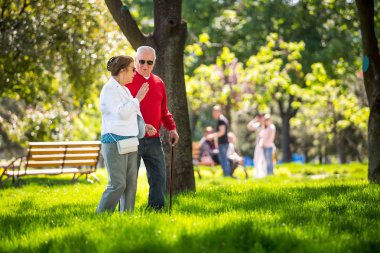 Neşeli son sınıf çifti şehir parkında eğleniyor, yürüyor, gülüyor ve güneşli günün tadını çıkarıyor. Yaşlı insanlar renkli kıyafetler giyiyorlar güneş gözlüğü takıyorlar.