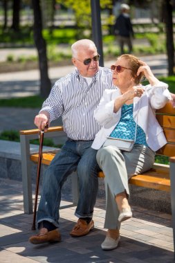 Şehir parkında bir bankta oturan rahatlatıcı sunlglasses giyen yaşlı çift