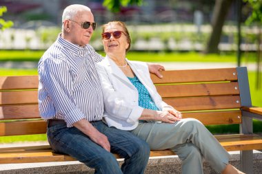 Şehir parkında bir bankta oturan rahatlatıcı sunlglasses giyen yaşlı çift
