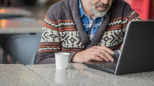 男人穿着秋天或冬天的衣服 围巾坐在咖啡店里用笔记本电脑工作 — 图库照片