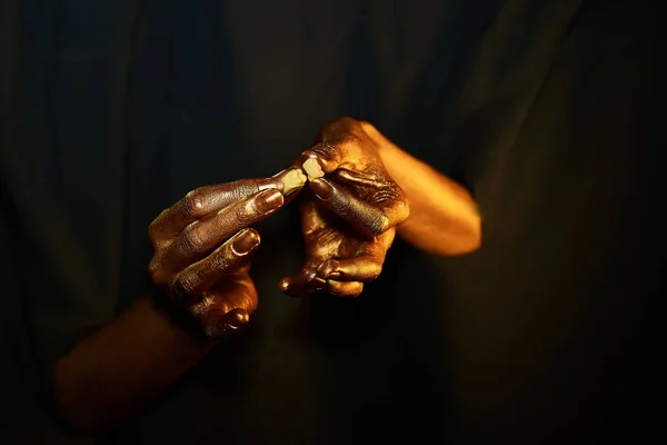two golden hands holding a tooth and a crown on a black background