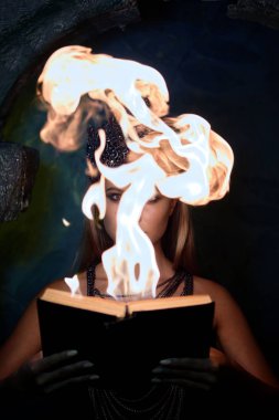 Gotik elbiseli kız yanan bir kitap karanlıkta tutar.