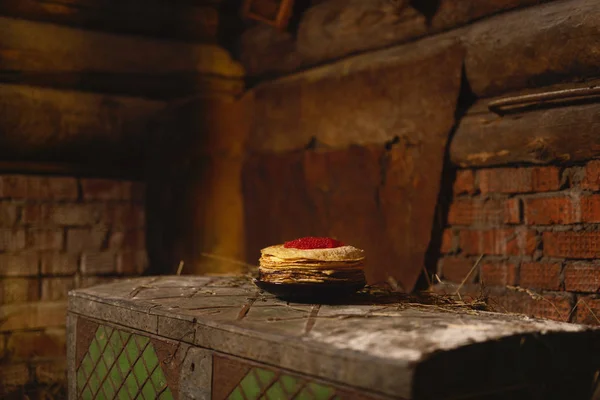 Una ragazza con pancake e caviale, in un kokoshnik rosso e giacca nera, si siede in un fienile . — Foto Stock