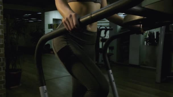 Piękna dziewczyna zajmuje się symulatorem w siłowni na czarnym tle — Wideo stockowe