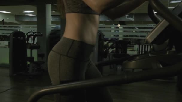 Belle fille engagée sur un simulateur dans la salle de gym sur un fond noir — Video