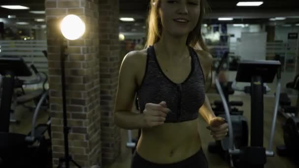 Belle fille engagée sur un simulateur dans la salle de gym sur un fond noir — Video