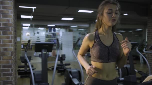 Vacker flicka engagerad på en simulator i gymmet på en svart bakgrund — Stockvideo