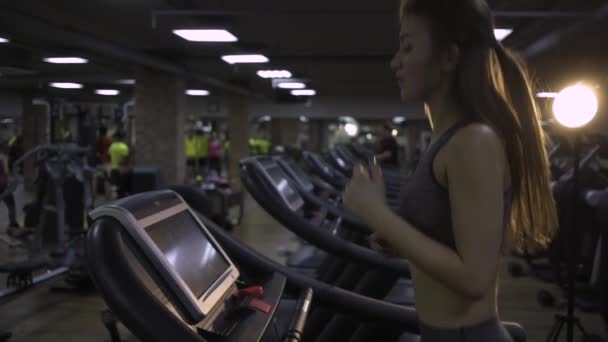 Menina bonita envolvida em um simulador no ginásio em um fundo preto — Vídeo de Stock