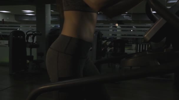 Belle fille engagée sur un simulateur dans la salle de gym sur un fond noir — Video