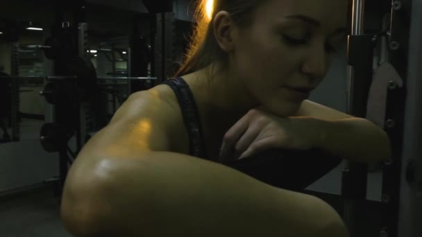 Hermosa chica comprometida en un simulador en el gimnasio sobre un fondo negro — Vídeo de stock