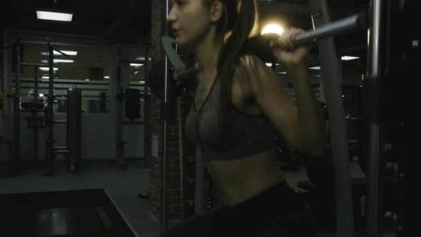 Mooi meisje betrokken op een simulator in de sportschool op een zwarte achtergrond — Stockvideo