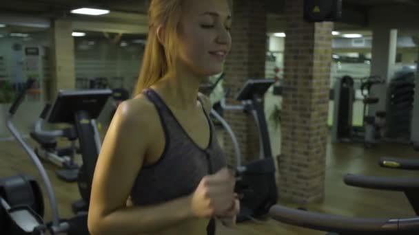 Belle fille engagée sur un simulateur dans la salle de gym sur un fond noir — Video