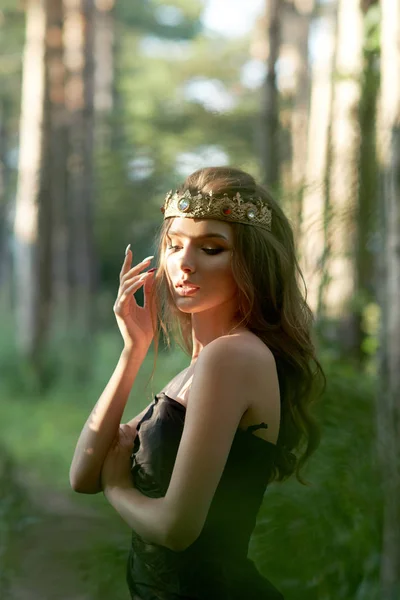 Молода, красива дівчина в чорній сукні з короною в лісі — стокове фото