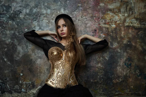 Fille dans une robe noire et un corset d'or contre un mur bleu — Photo