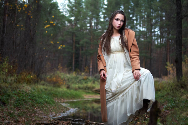 Girl in a white dress and a brown coat in the autumn