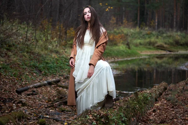 Meisje in een witte jurk en een bruine jas in de herfst bos — Stockfoto