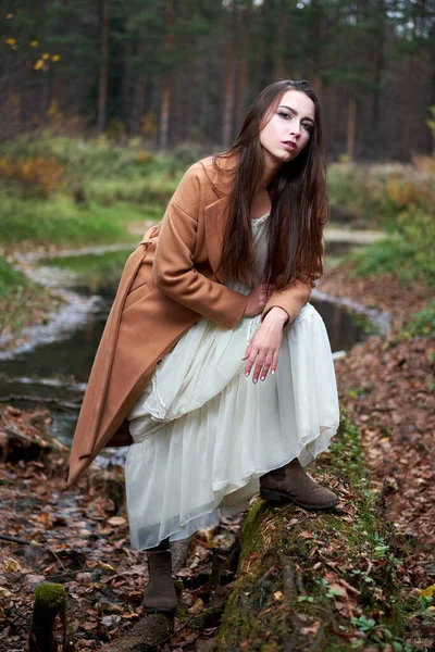 Flicka i vit klänning och brun rock i höstskogen — Stockfoto