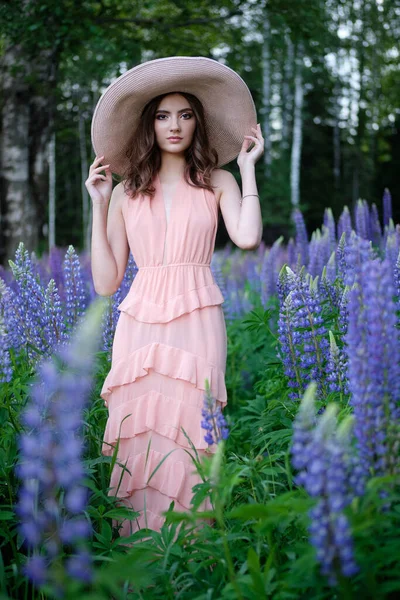 Blond glimlachende jonge vrouw met een lupine boeket op de achtergrond van de natuur. Het concept van schoonheid en romantiek. — Stockfoto