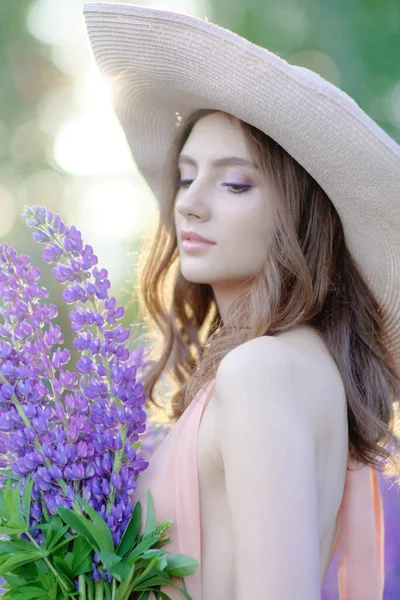 Blond glimlachende jonge vrouw met een lupine boeket op de achtergrond van de natuur. Het concept van schoonheid en romantiek. — Stockfoto