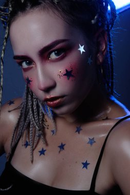 Siyah bluzlu, yaratıcı makyajlı, mavi ışıklı kız stüdyoda poz veriyor.