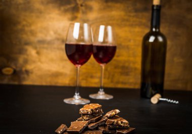 bir şişe şarap, çikolatalı dilimler ve iki bardak koyu arka plan üzerinde