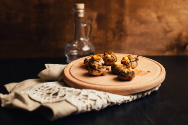 Mantar kapaklar peynir ve et ile doldurulmuş, fırında pişmiş ve ince dal dereotu ile süslenmiş. Ahşap tahta üzerinde mantar meze. Portre