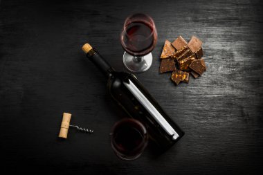 Kırmızı şarap ile bir tirbuşon bir şişe. Siyah bir ahşap arka plan üzerinde.