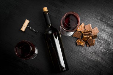 Kırmızı şarap ile bir tirbuşon bir şişe. Siyah bir ahşap arka plan üzerinde.