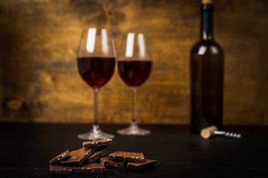 bir şişe şarap, çikolatalı dilimler ve iki bardak koyu arka plan üzerinde