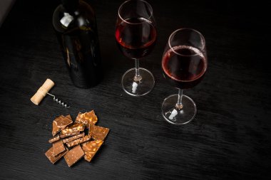 Kırmızı şarap ile bir tirbuşon bir şişe. Siyah bir ahşap arka plan üzerinde.