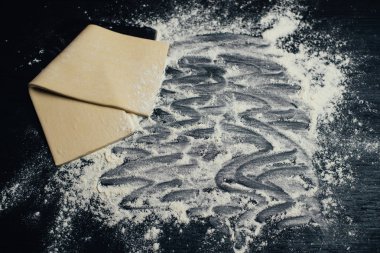 Puf böreği hamuru. Ev yapımı katlanmış ham puf böreği bir tablo. Puf böreği yapma. Hamur'ın bir oklava ile rulo ve kopya alanı ile un.