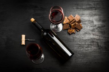 Kırmızı şarap ile bir tirbuşon bir şişe. Siyah bir ahşap arka plan üzerinde.