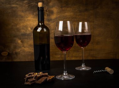 bir şişe şarap, çikolatalı dilimler ve iki bardak koyu arka plan üzerinde