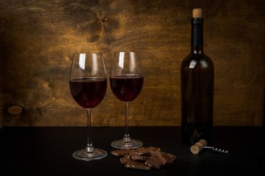 bir şişe şarap, çikolatalı dilimler ve iki bardak koyu arka plan üzerinde