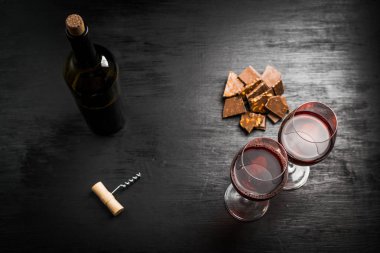 bir şişe şarap, çikolatalı dilimler ve iki bardak koyu arka plan üzerinde