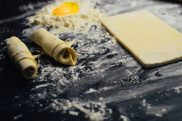 Ingredients and utensils for the preparation of bakery products - flour, dough, egg, rolling pin, whisk, strainer, bread - on black table with free copy space