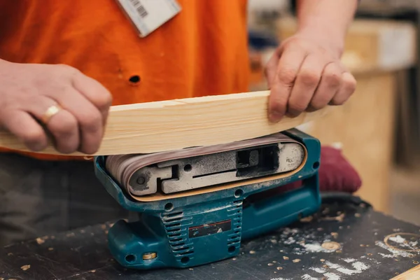 Man sanding a wood with sander in a workshop